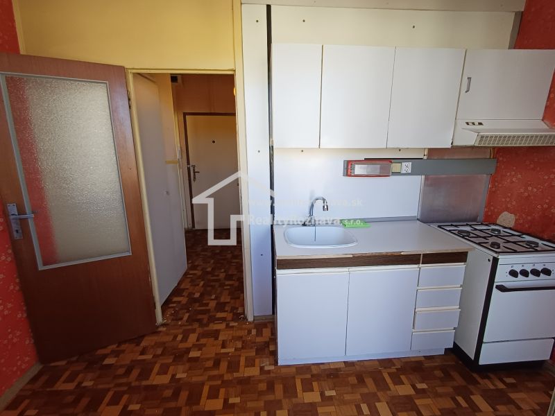 A kitchen in a studio apartment with a wood-patterned floor and white cabinetry.