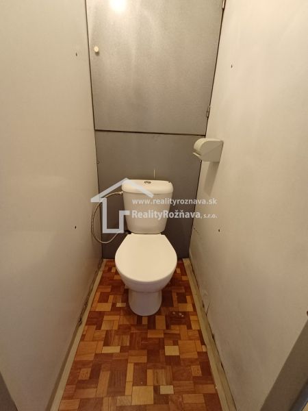 A bathroom in a one-room apartment with a wooden decor floor.