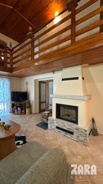 Interior of a cabin with a fireplace and a gallery, wooden decor flooring and a TV corner.
