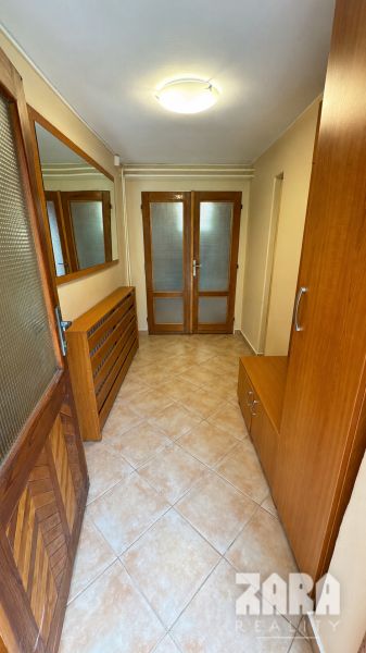 A hallway in a cabin with ceramic tiles, wooden furniture, and glass doors.
