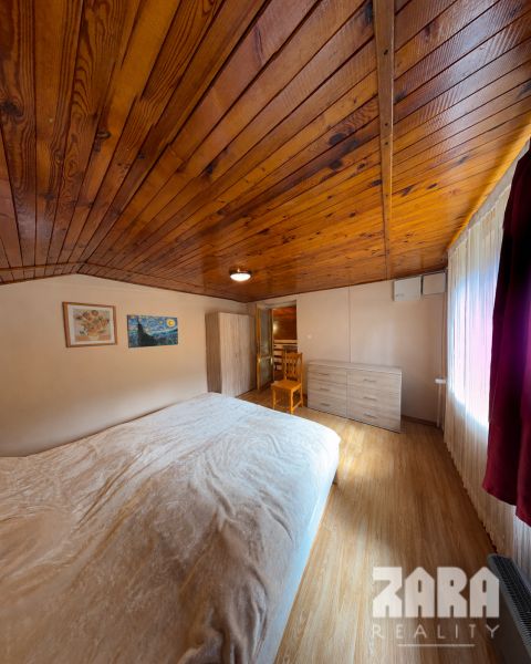 A room in a cottage with a wooden ceiling, a floor with a wooden decor, furniture, and a bed.