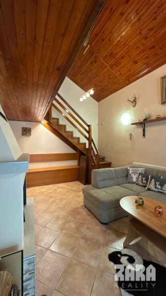 Interior of a cabin with a wooden floor, a sofa, a staircase, and decorations.