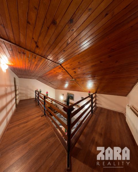 The attic of the cottage with a wooden decor floor and a wooden ceiling.