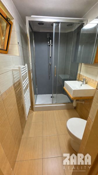Bathroom with a toilet, shower, sink, and tiles in a cabin with a wooden decor floor.
