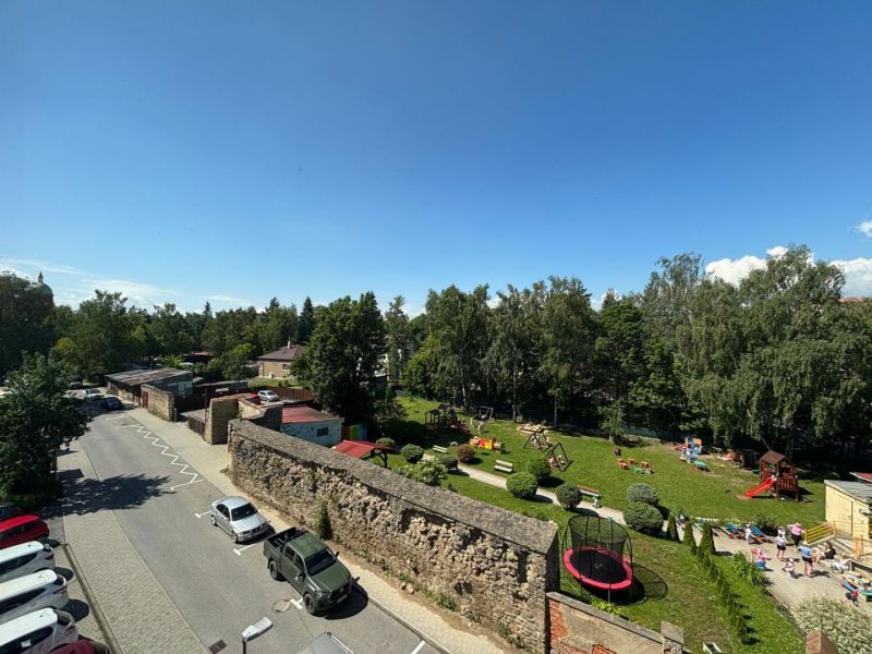 A street with cars and a wall near the park in Kežmarok, offices close to greenery.