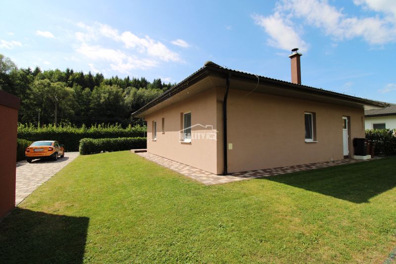 A family house in Bytča with a lawn, paving, and an access road, surrounded by greenery.