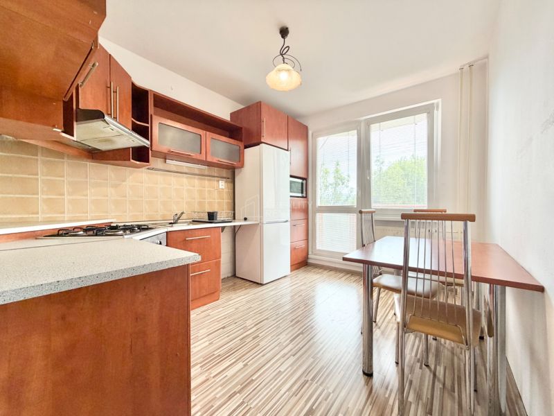 A kitchen in a 2-room apartment with a wooden decor floor, a dining table, and appliances.