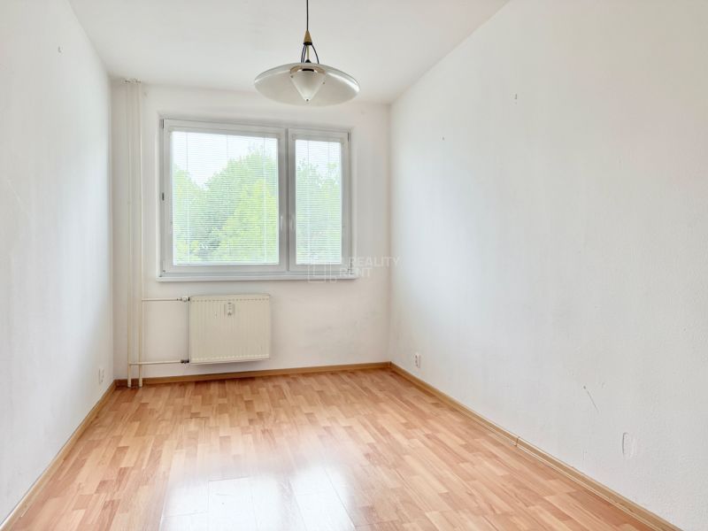 A room in a 2-room apartment with a wooden decor floor and a large window.