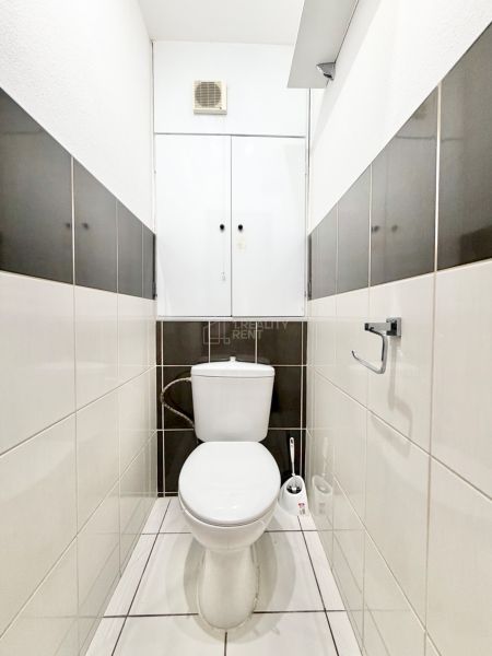 Bathroom with toilet in a 2-room apartment with light tiles and a towel rack.