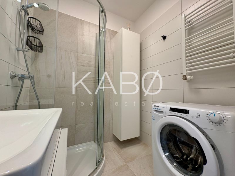 A bathroom in a 2-room apartment with a sink, shower, and washing machine.