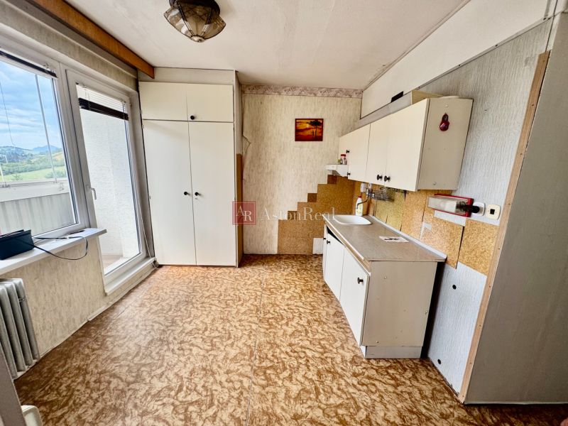 A kitchen in a 2-room apartment with white furniture and a wooden decor floor.
