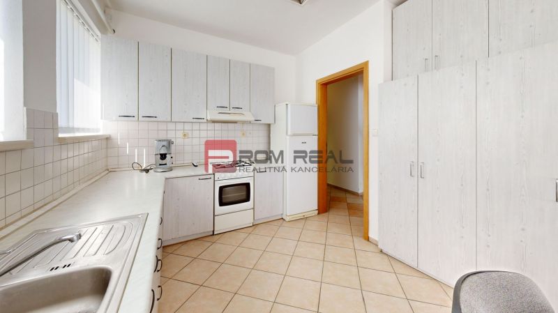 A kitchen area in a production facility with white cabinets, a sink, and a tiled floor.