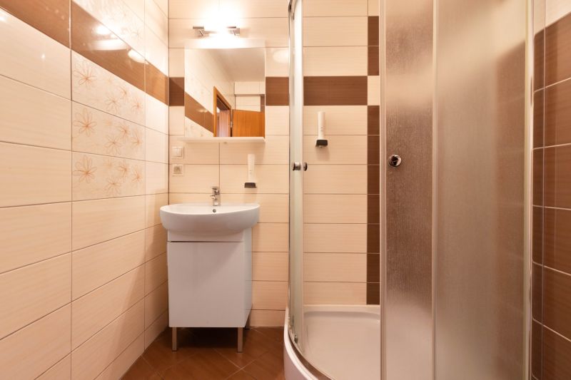 Bathroom in a 2-room apartment with a sink and a shower with brown tiles.