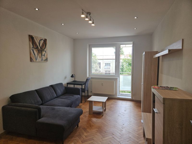 A comfortable living room with a sofa, a desk, and a wooden decor floor in a two-room apartment.