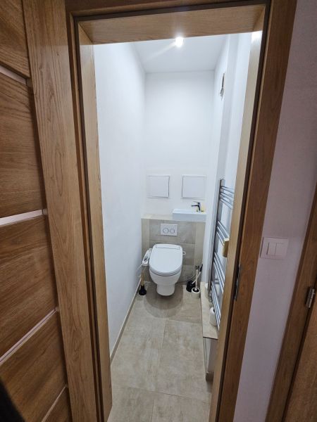 Compact toilet with ceramic tiles and a white sink in a 2-room apartment.