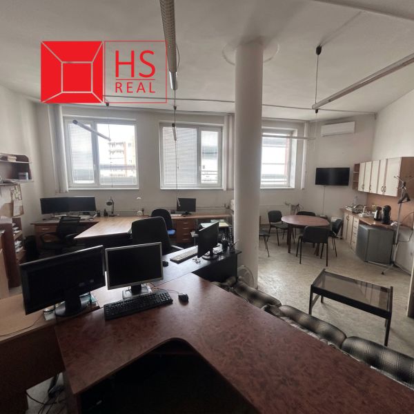 In an office with a wooden decor floor, there are desks, computers, and a kitchenette.