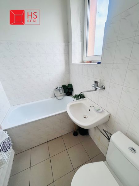 A bathroom with a bathtub, sink, and toilet, tiled with light tiles.