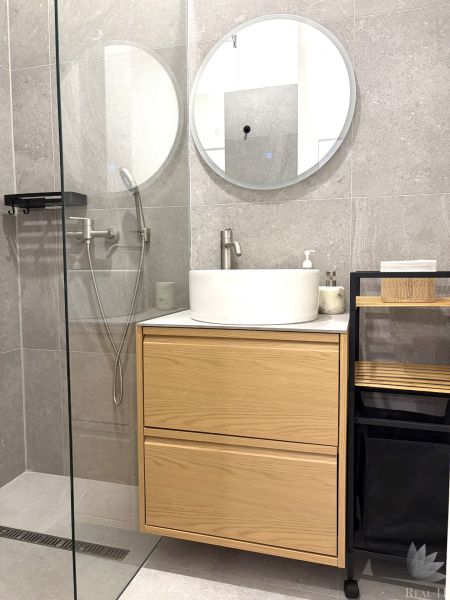 A bathroom in a 3-room apartment with a sink on a wooden cabinet and a round mirror.