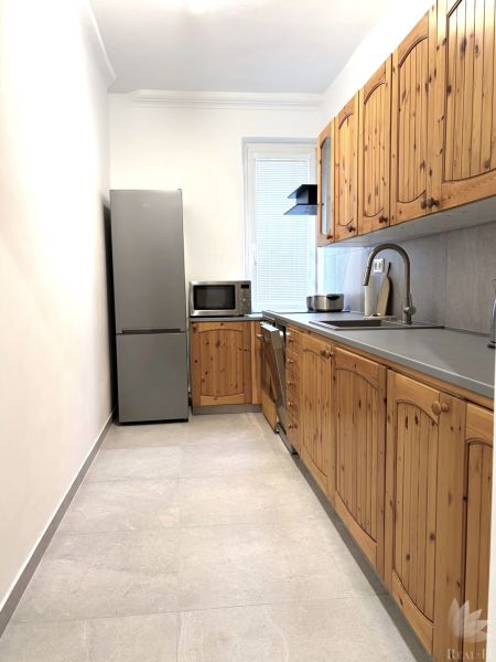 A kitchen with wooden cabinets, a white wall, and light tiles in a three-room apartment.