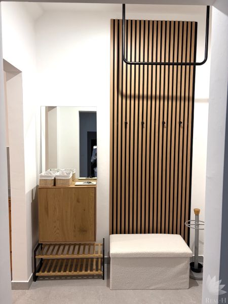 Hallway with a coat rack wall and a bench in a 3-room apartment with a wooden decor floor.