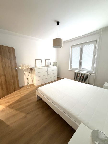 A bedroom with light walls, a bed, and a floor with a wood decor in a 3-room apartment.