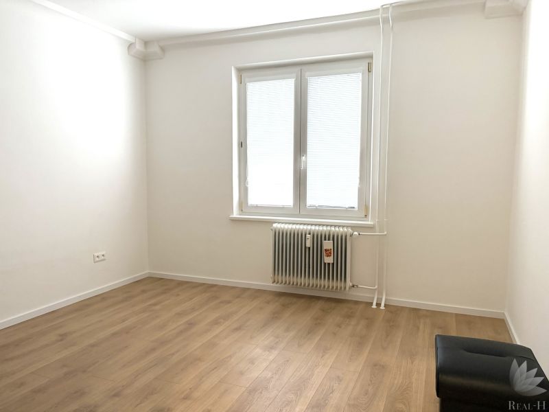White room with a wood-patterned floor in a 3-room apartment with a radiator.