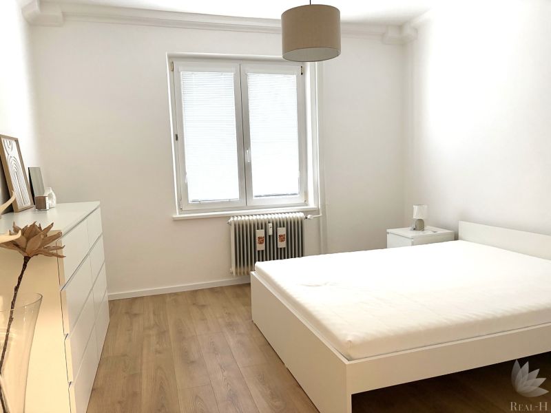 A bedroom in a 3-room apartment with a wooden decor floor and a window with blinds.