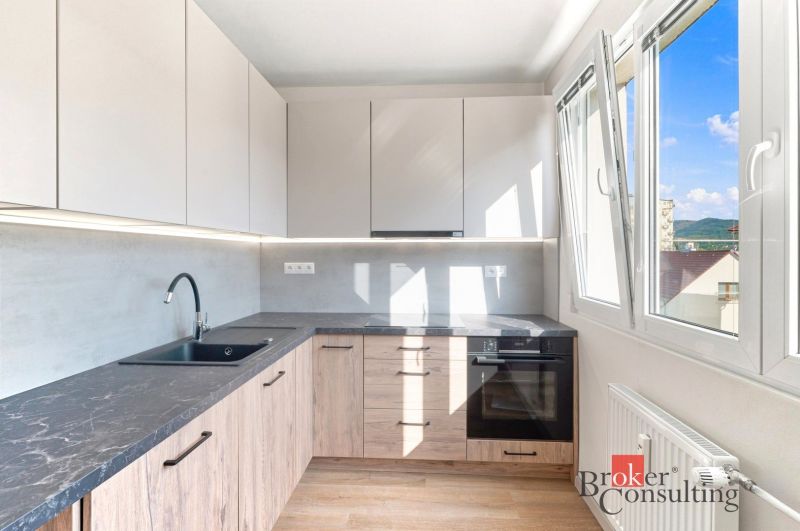 A kitchen of a 2-room apartment with large windows and a countertop with a wooden decor.