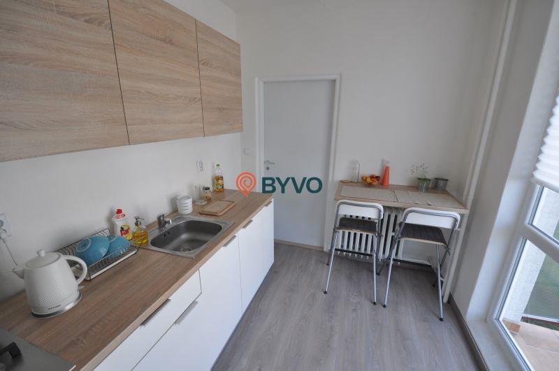A kitchen with a wood-patterned floor in a 2-room apartment, with a dining table and chairs.