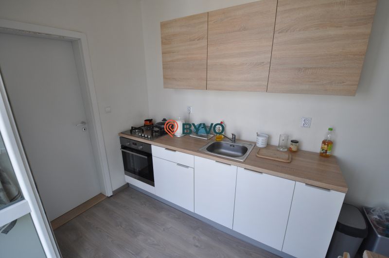 A kitchen in a 2-room apartment with a wood-patterned floor, white cabinets, and a stove.