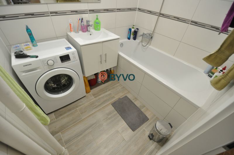 A bathroom in a 2-room apartment with a bathtub, washing machine, and cabinet.