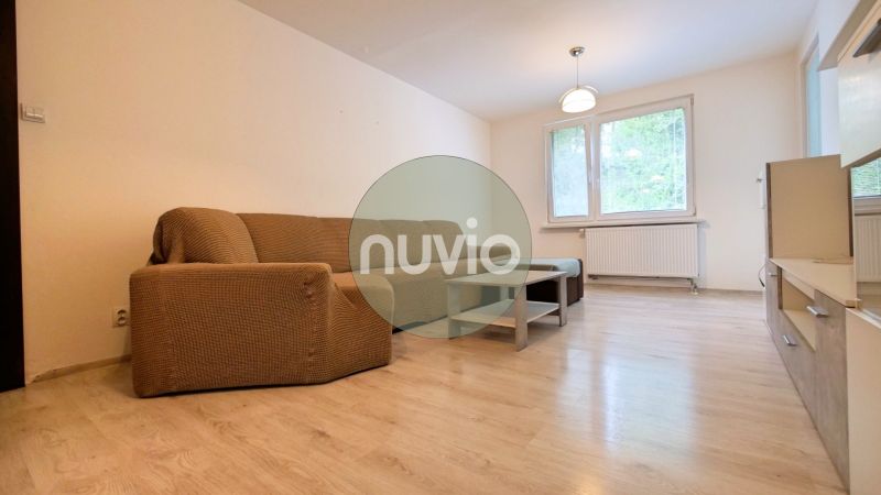 Living room with a sofa and wood-patterned flooring in a three-room apartment.