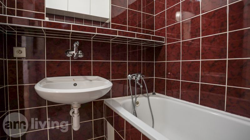 A bathroom in a 2-room apartment with dark tiles, a sink, and a bathtub.