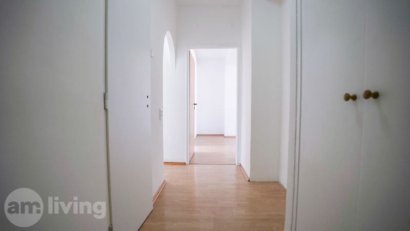 A hallway with a wooden decor floor and white walls in a 2-room apartment.