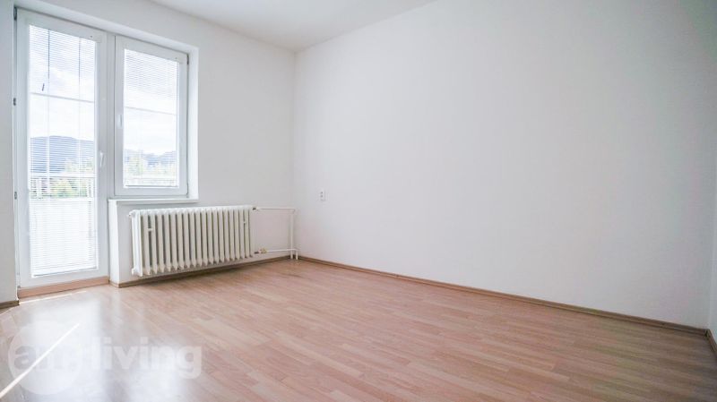 A room in a 2-room apartment with a wooden decor floor, white wall, radiator.