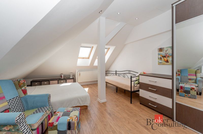 Attic room with a bed, chair, and wooden decor flooring in a 3-room apartment.