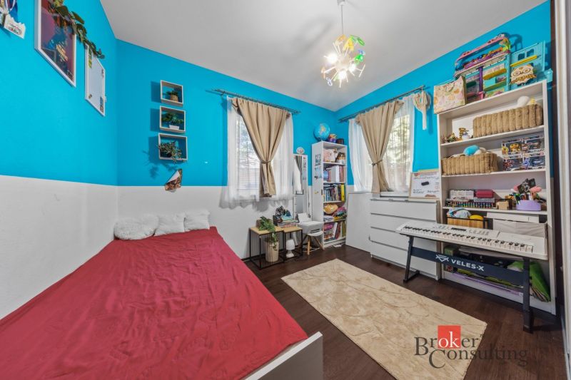 A children's room with colorful walls, a bed, a piano, and shelves full of toys and books.