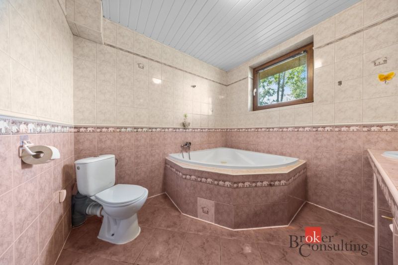 A bathroom in a family house with a corner bathtub and a side window.