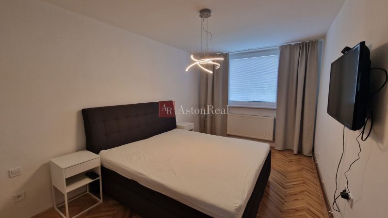Bedroom in a 3-room apartment with a bed, television, and wooden decor flooring.