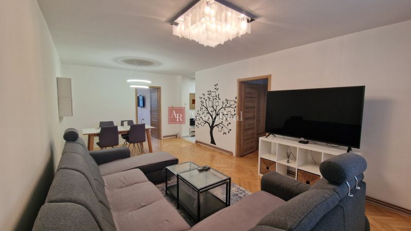 Living room with a large TV, gray sofa, and wooden decor flooring in a 3-room apartment.