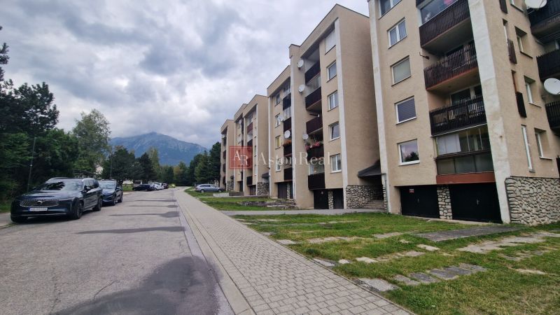 Apartment building on Pod lesom Street, Vysoké Tatry, surrounded by mountains and parked cars.