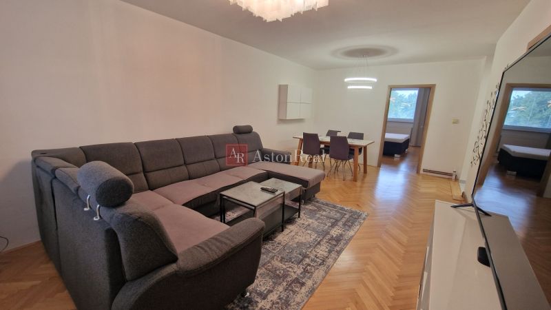 Spacious living area in a 3-room apartment with a sofa and a dining table, floor with wood decor.
