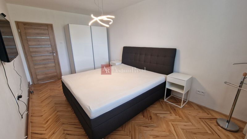 Bedroom with a double bed, white wardrobe, and wooden decor flooring in a 3-room apartment.