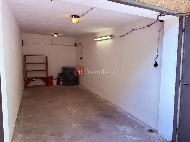 Inside the garage, there is a concrete floor, a shelf, and ceiling lighting.