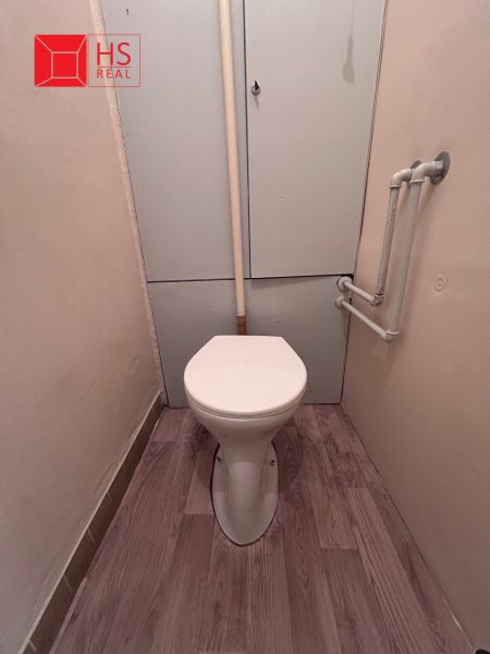 A toilet with a wooden decor floor in a 2-room apartment.
