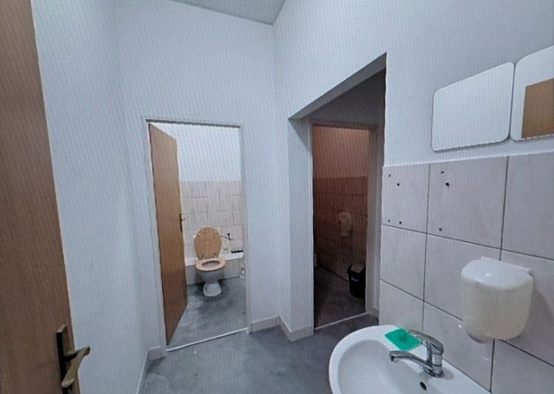 Sink and toilet in offices with white tiles and gray flooring.