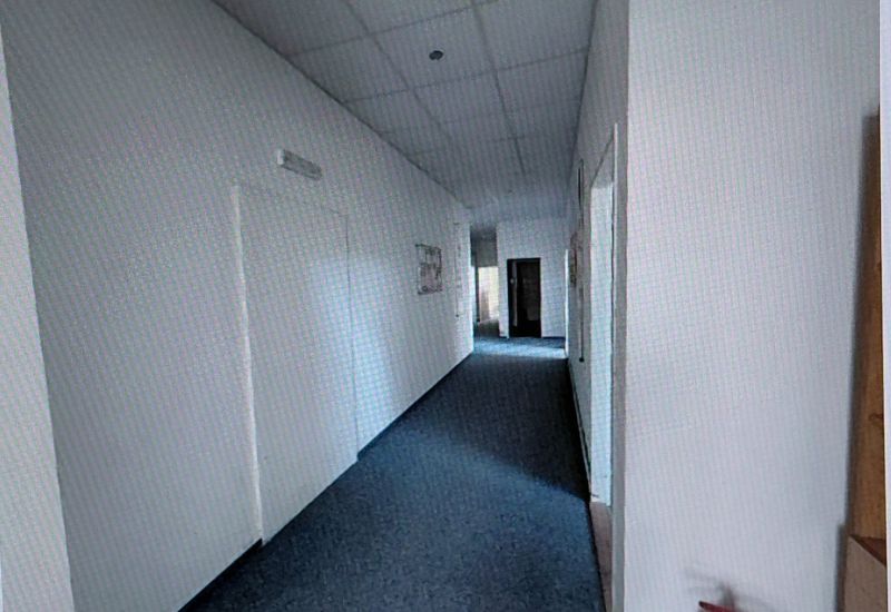 A narrow hallway with light walls and carpet in an office.
