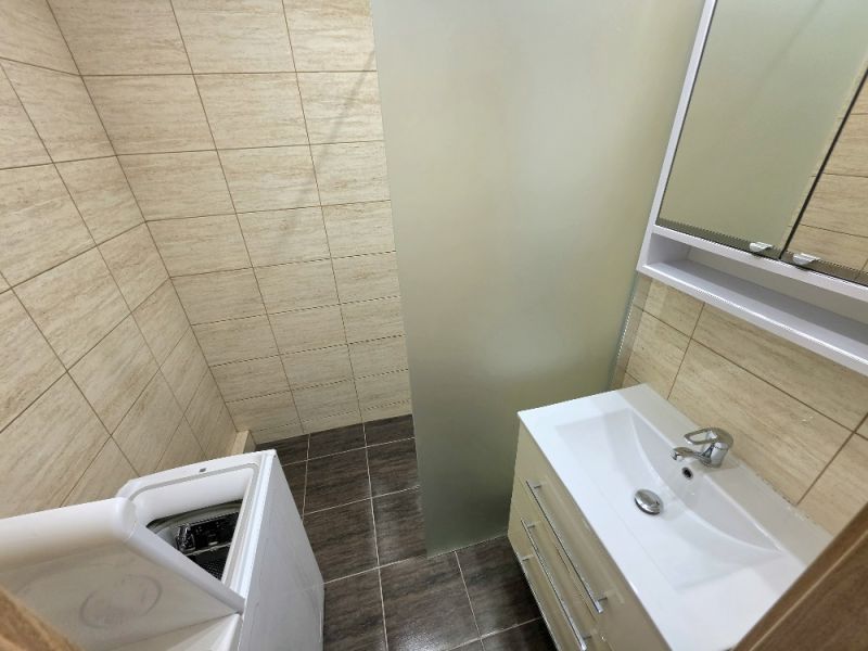Bathroom in a 3-room apartment with a washing machine, sink, and beige tiles.