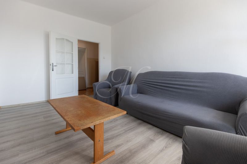 Living room with a sofa, an armchair, a wooden table, and a wooden-patterned floor in a 3-room apartment.