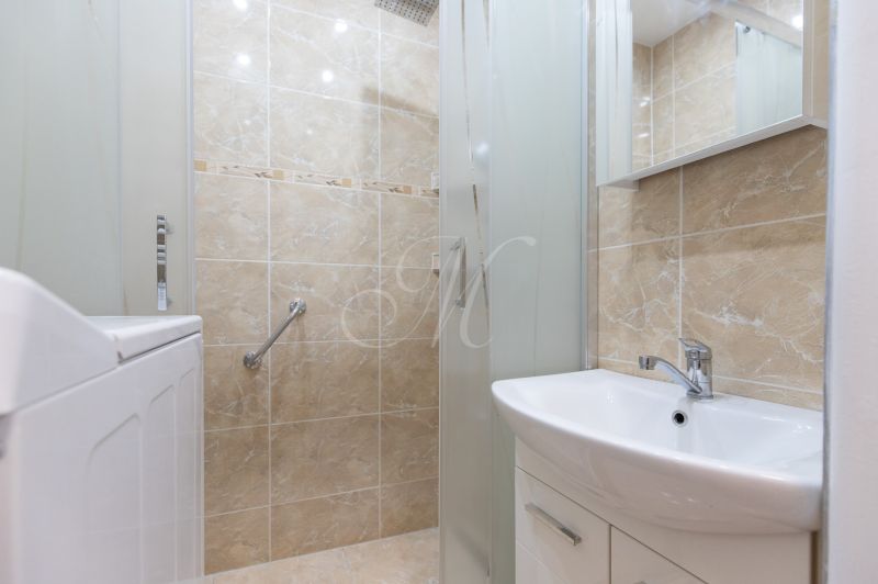 A bathroom in a 3-room apartment with a sink, a shower corner, and beige tiles.